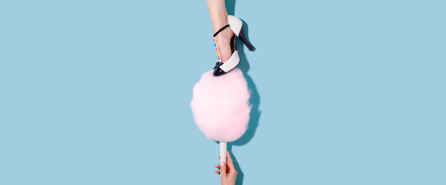 Woman's shoe stepping on pink fairy floss against blue background