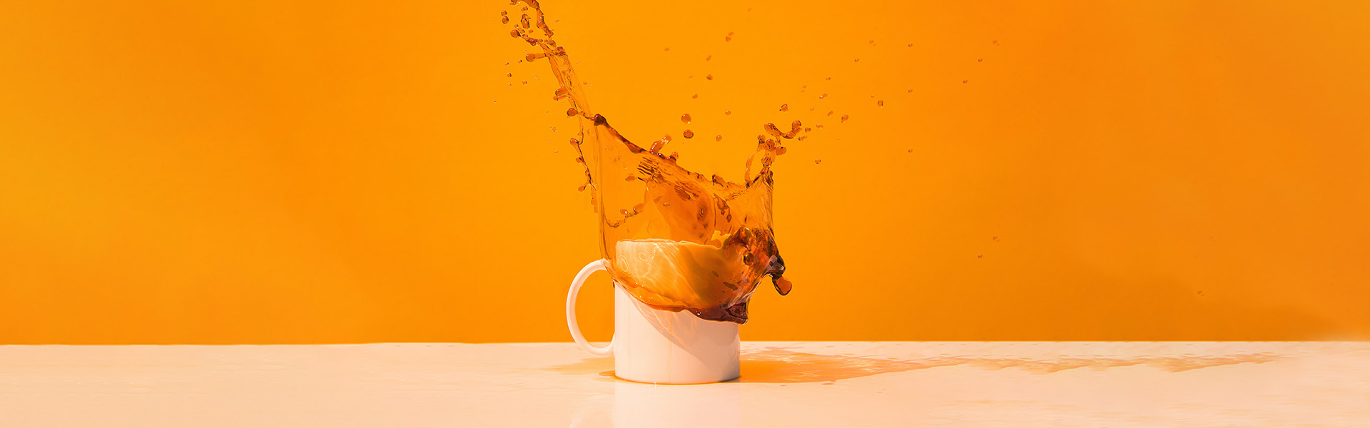 coffee mug with coffee splash against orange background