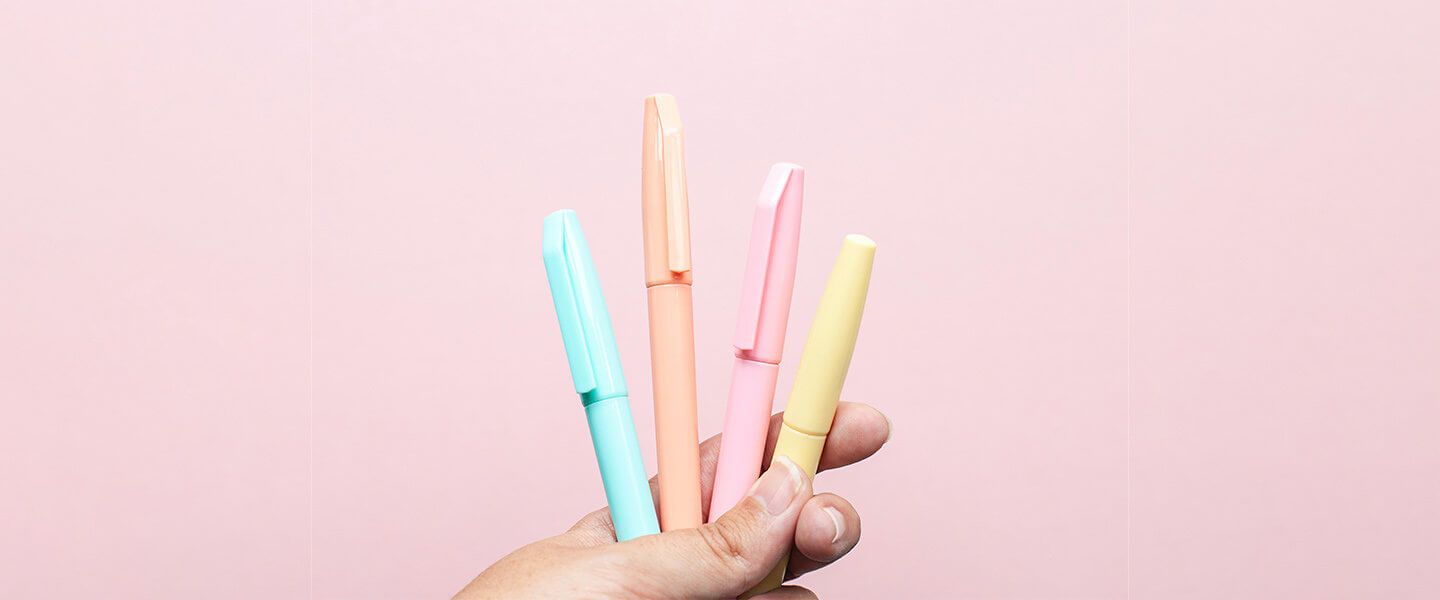 Hand holding group of pens against pink background