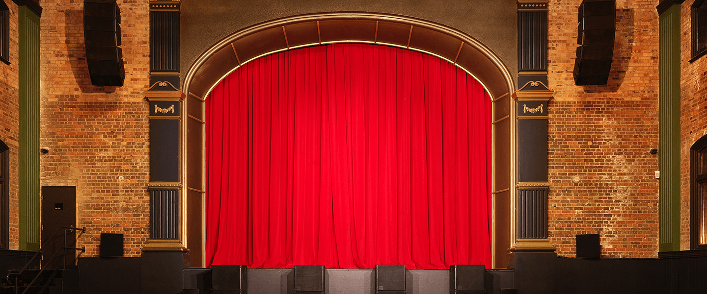 Image of an empty theatre with red stage curtain