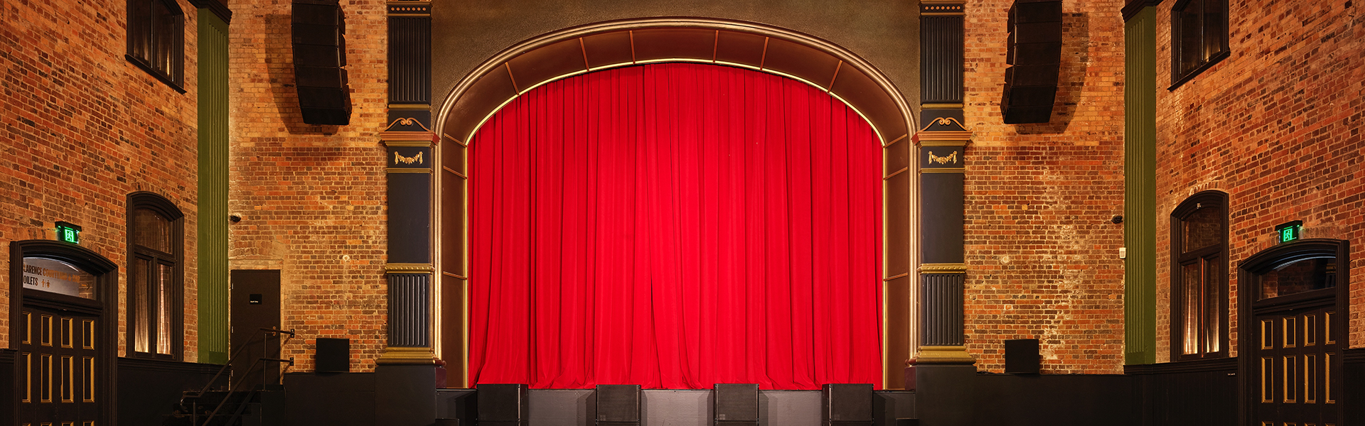 Image of an empty theatre with red stage curtain