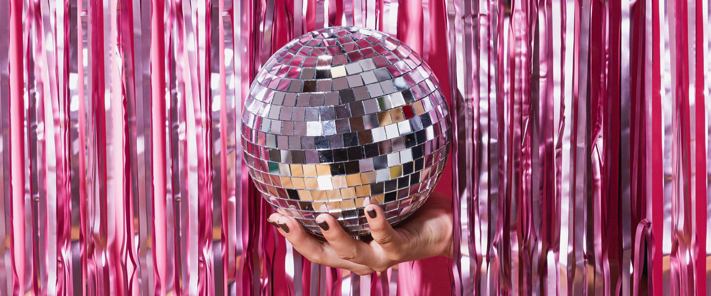 Hand holding mirrorball against pink tinsel background