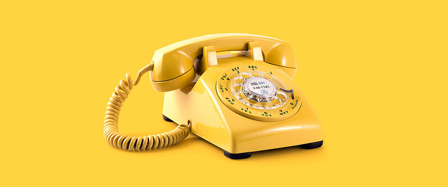 Yellow rotary telephone against yellow background