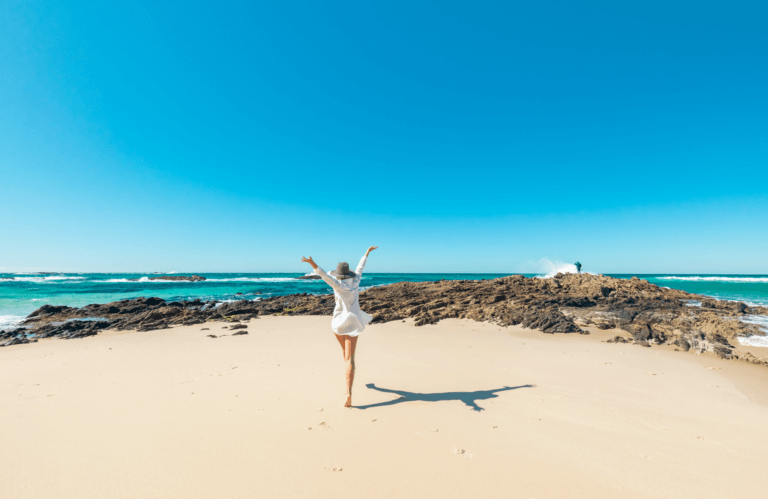 Woman on North Stradbroke Island beach wearing white with her arms raised