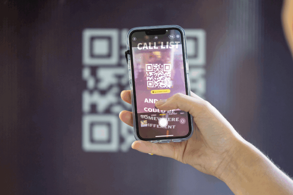 Close-up of a smartphone scanning a QR code on the Queensland-branded phone booth, promoting the Queensland is Calling campaign.
