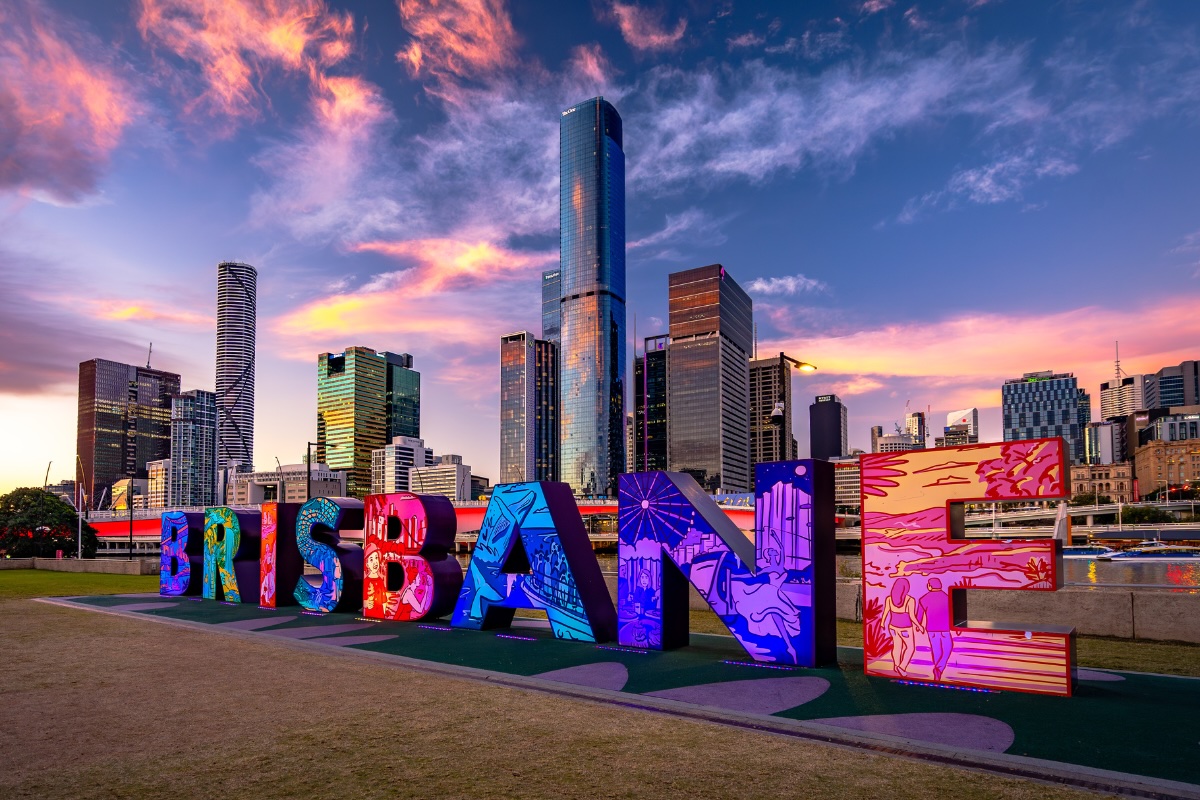 Brisbane sign at Southbank Parklands lit up with city in background.