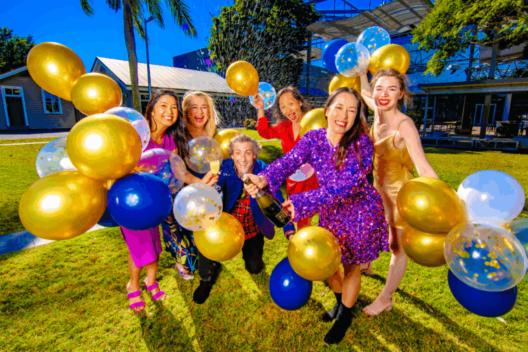 La Boite creatives pose to celebrate 100 years, with colourful outfits, balloons and champagne.