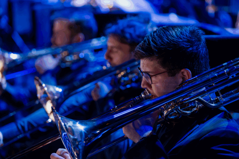 Photos shows QSO's brass section, with trumpets mid concert under a blue light.