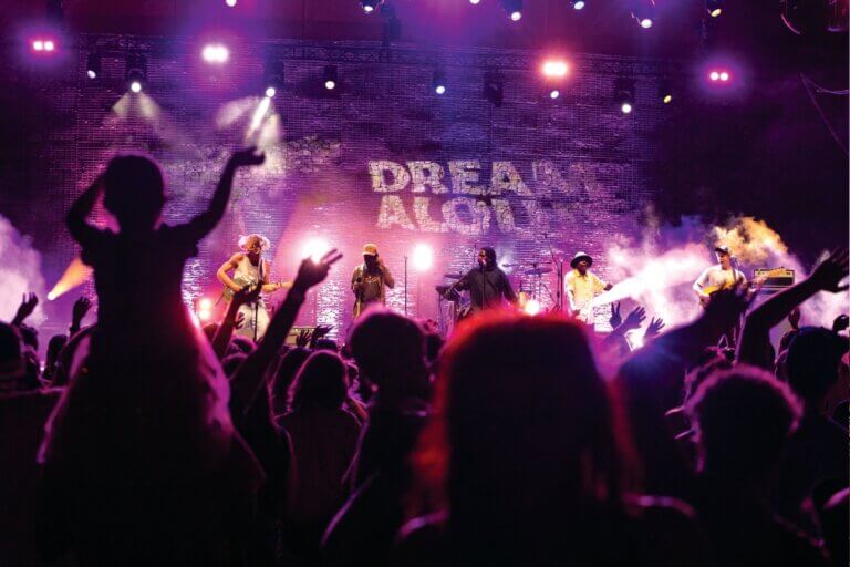 Purple stage with 'Dream Aloud' written on it. Performers lit by stage lights look towards the audience.