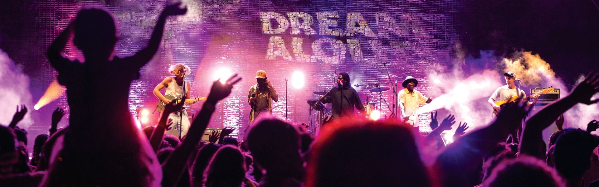 Purple stage with 'Dream Aloud' written on it. Performers lit by stage lights look towards the audience.