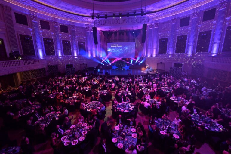 Brisbane City Hall at 2024 Lord Mayor's Business Awards. Stage illuminated with blue, pink and purple lights. Audience with guests seated at round tables.