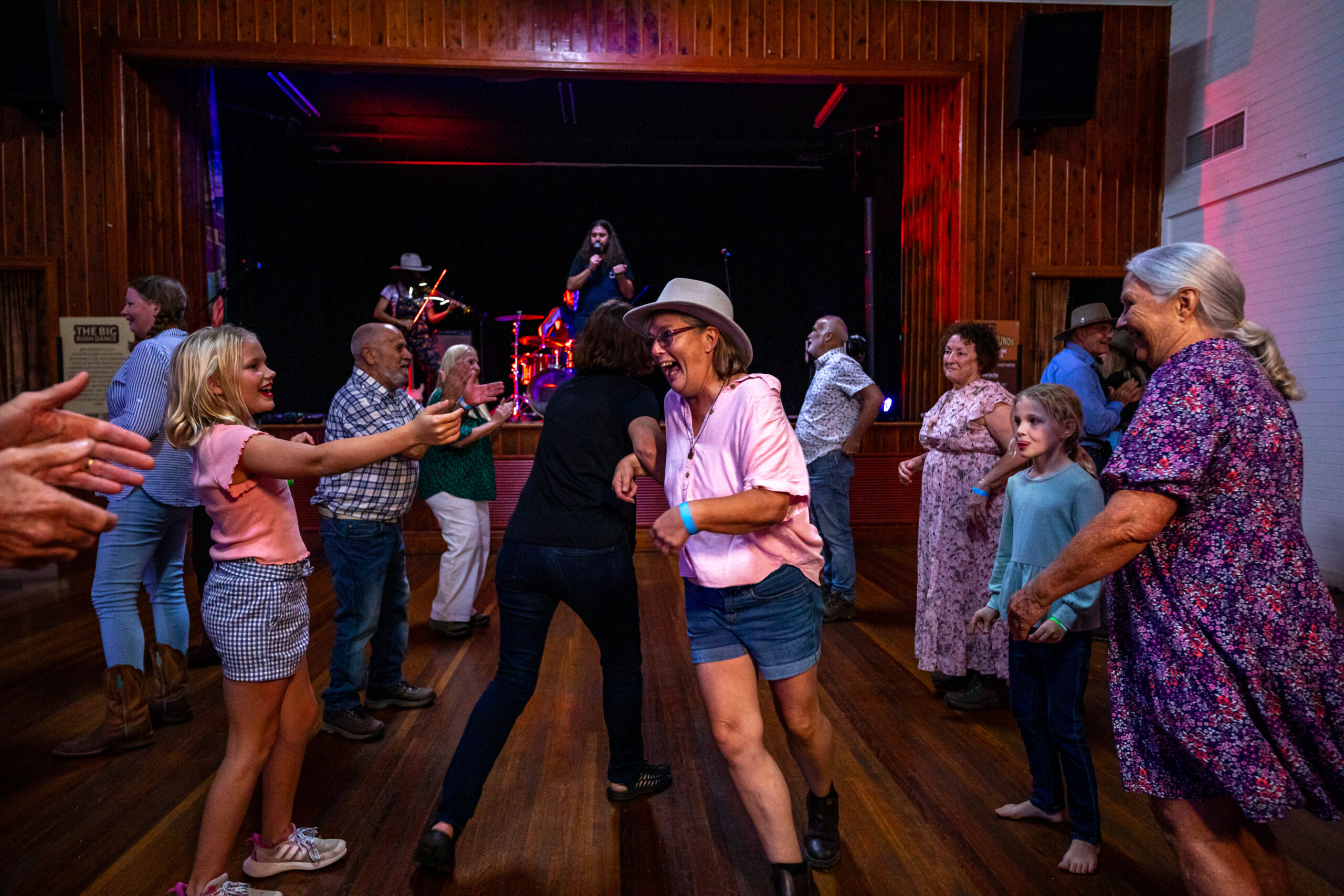 A dance floor with people smiling and interacting and illuminated by pink lights.
