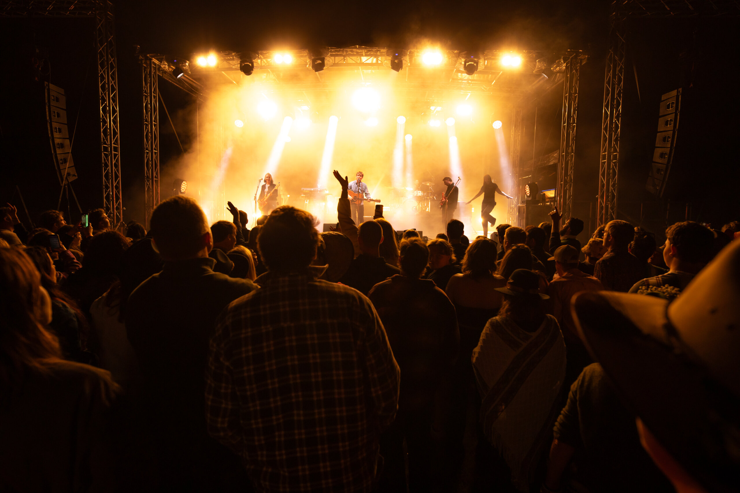 A stage illuminated by bright yellow lights with a dimmed crowd cheering in front.